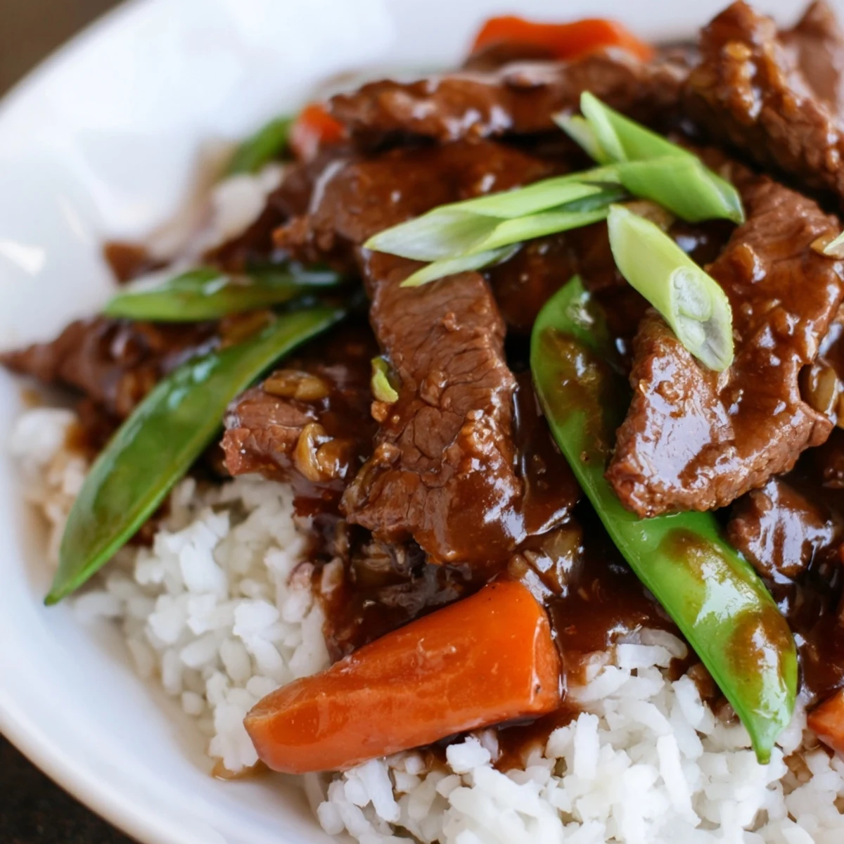 A close-up of sizzling Beef Stir Fry with Snow Peas and Carrots, featuring saucy beef, vibrant orange carrots, and fresh green pods.