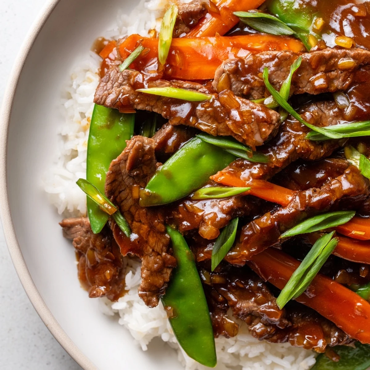 Freshly plated Beef Stir Fry with Snow Peas and Carrots served over steamed rice, garnished with sliced spring onions for a colorful weeknight meal.