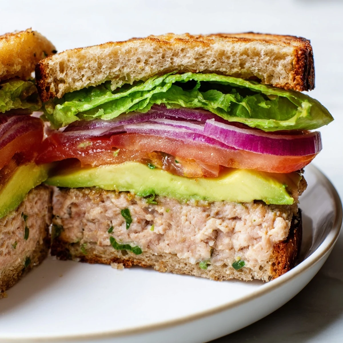 Stacked turkey burger with creamy avocado slices, fresh lettuce, and juicy tomato on a bun.