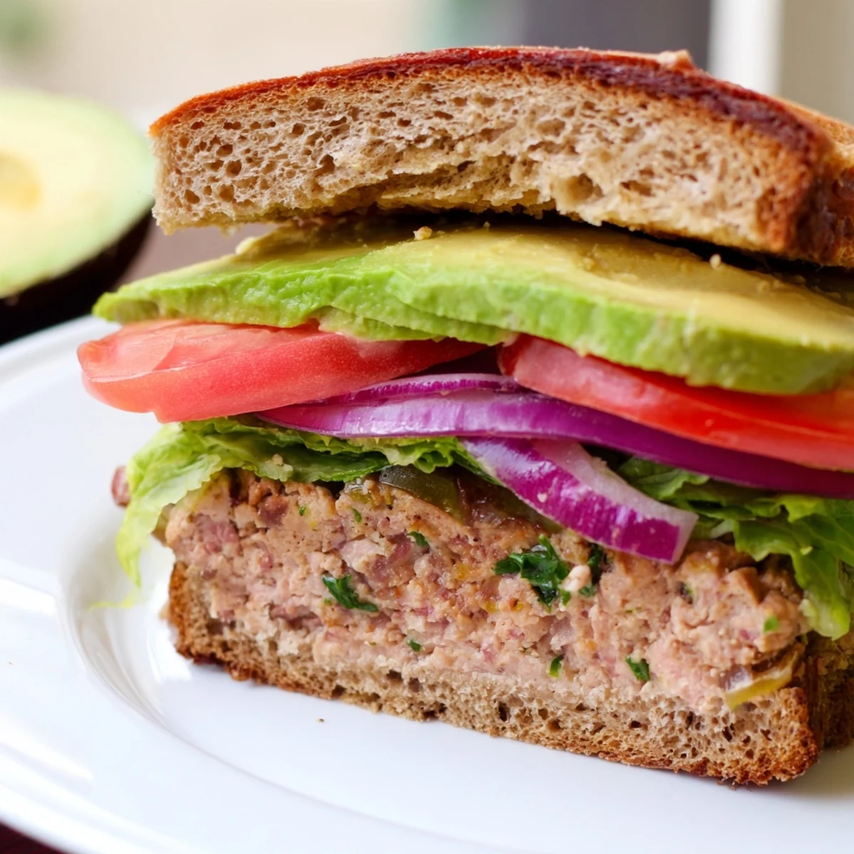 Turkey Burger with Avocado on a toasted whole wheat bun with tomato and red onion slices.