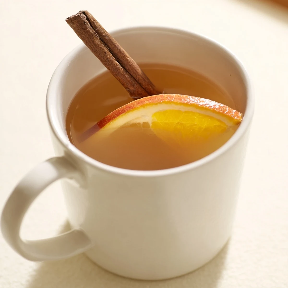 Steaming mugs of spiced hot apple juice with cinnamon glow warmly beside orange slices and whole spices.
