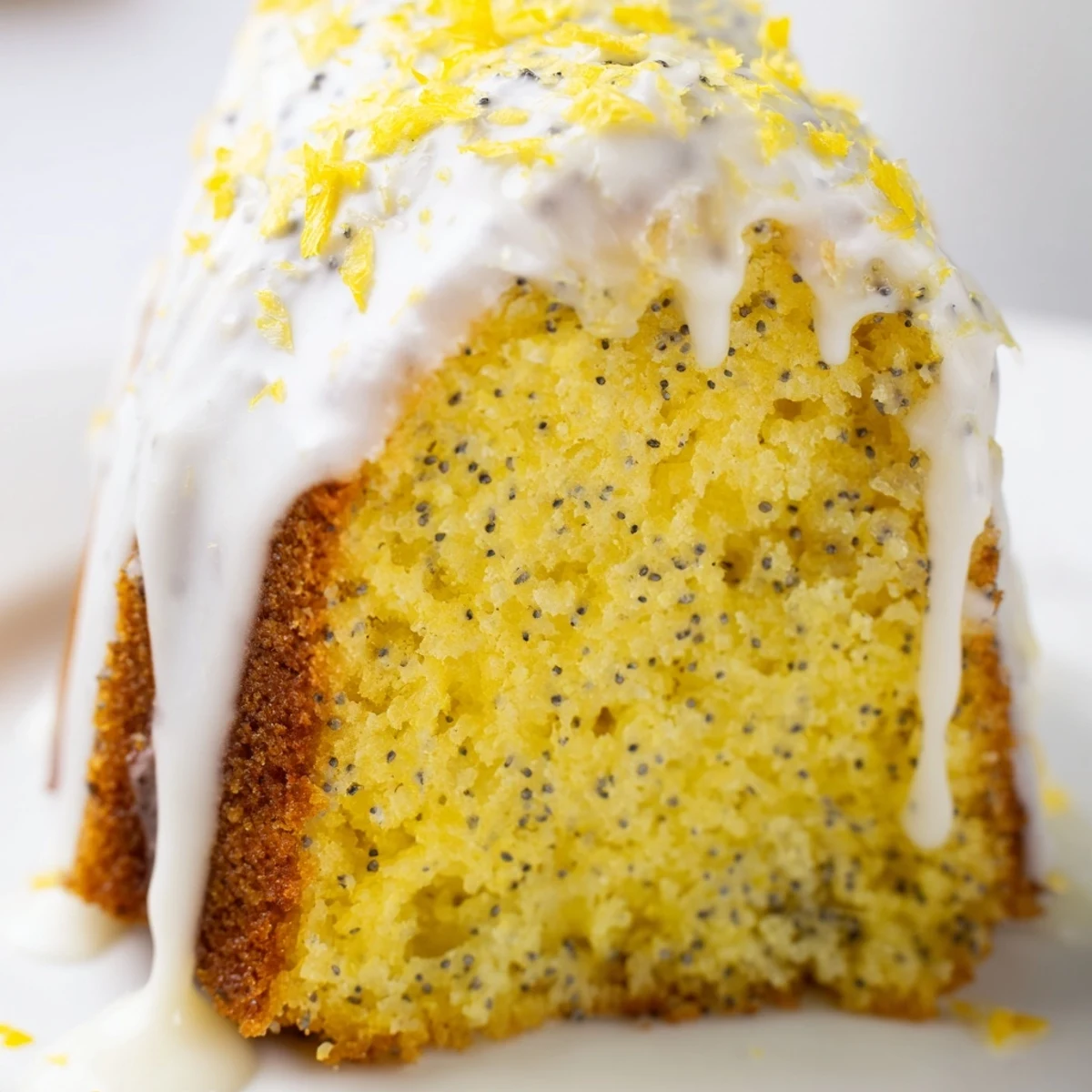 A slice of moist Lemon Poppy Seed Bundt Cake on a white plate, revealing tender crumb and poppy seeds beside a lemon wedge.