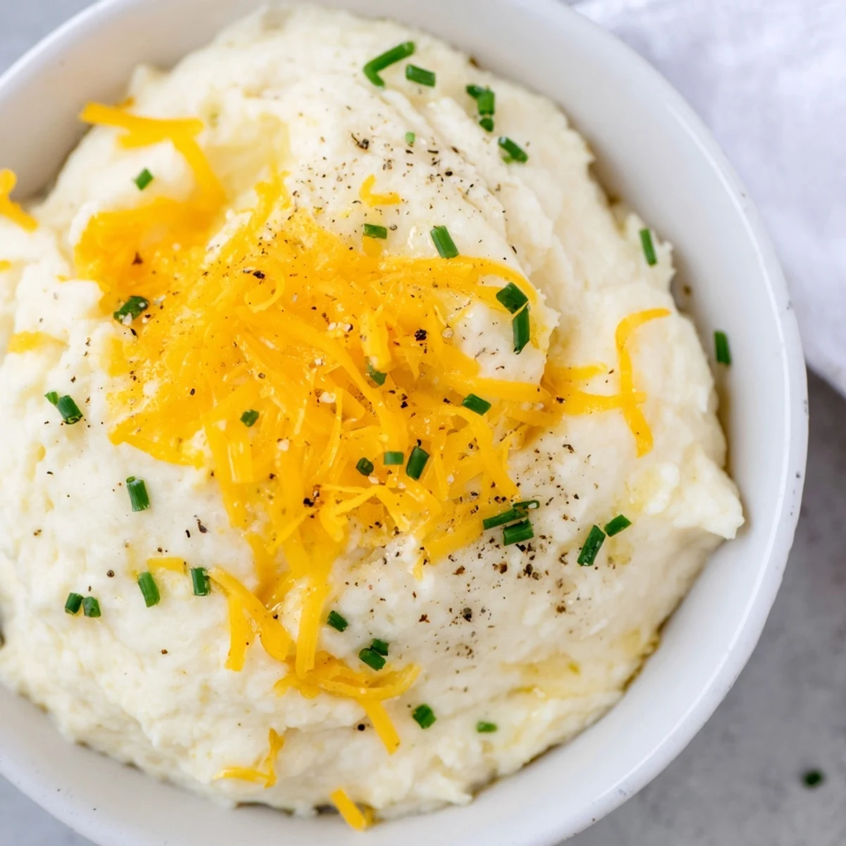 A comforting bowl of Garlic Mashed Cauliflower with Cheese, featuring tender cauliflower florets blended with roasted garlic for a velvety texture.