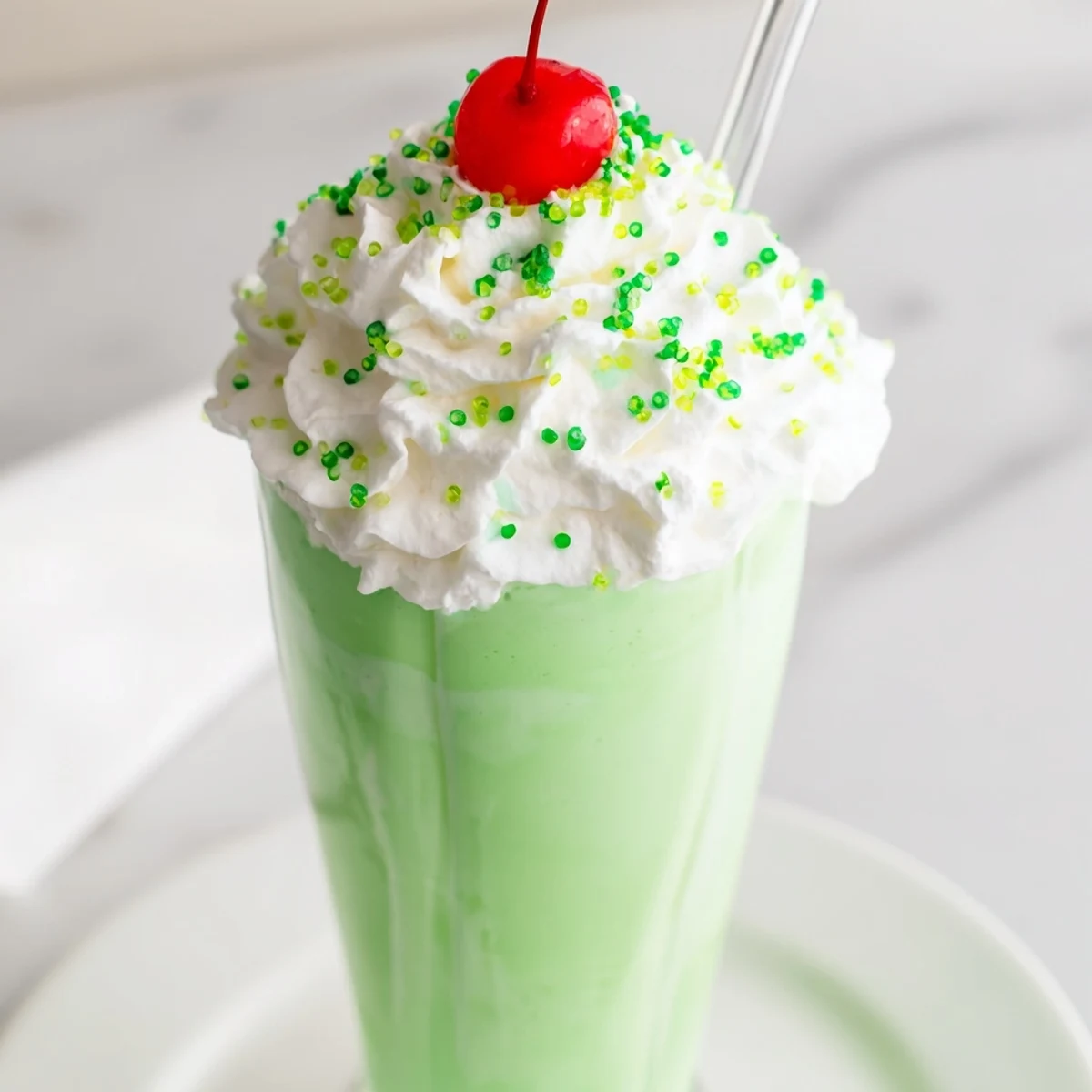 Creamy Shamrock Mint Milkshake topped with whipped cream and green sprinkles, served in a tall glass with a straw.