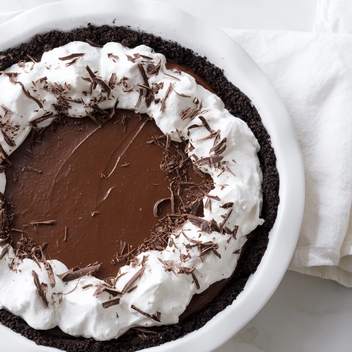 Decadent Romantic Chocolate Silk Pie slice on a plate, featuring a chocolate cookie crust and airy whipped cream topping.