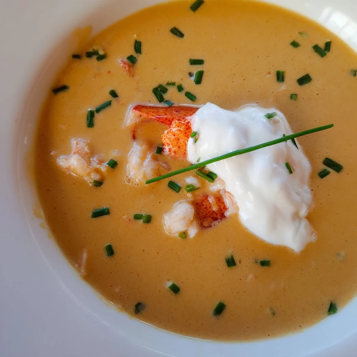 Close-up of Romantic Lobster Bisque with crème fraîche garnish and a glass of crisp Chardonnay nearby.