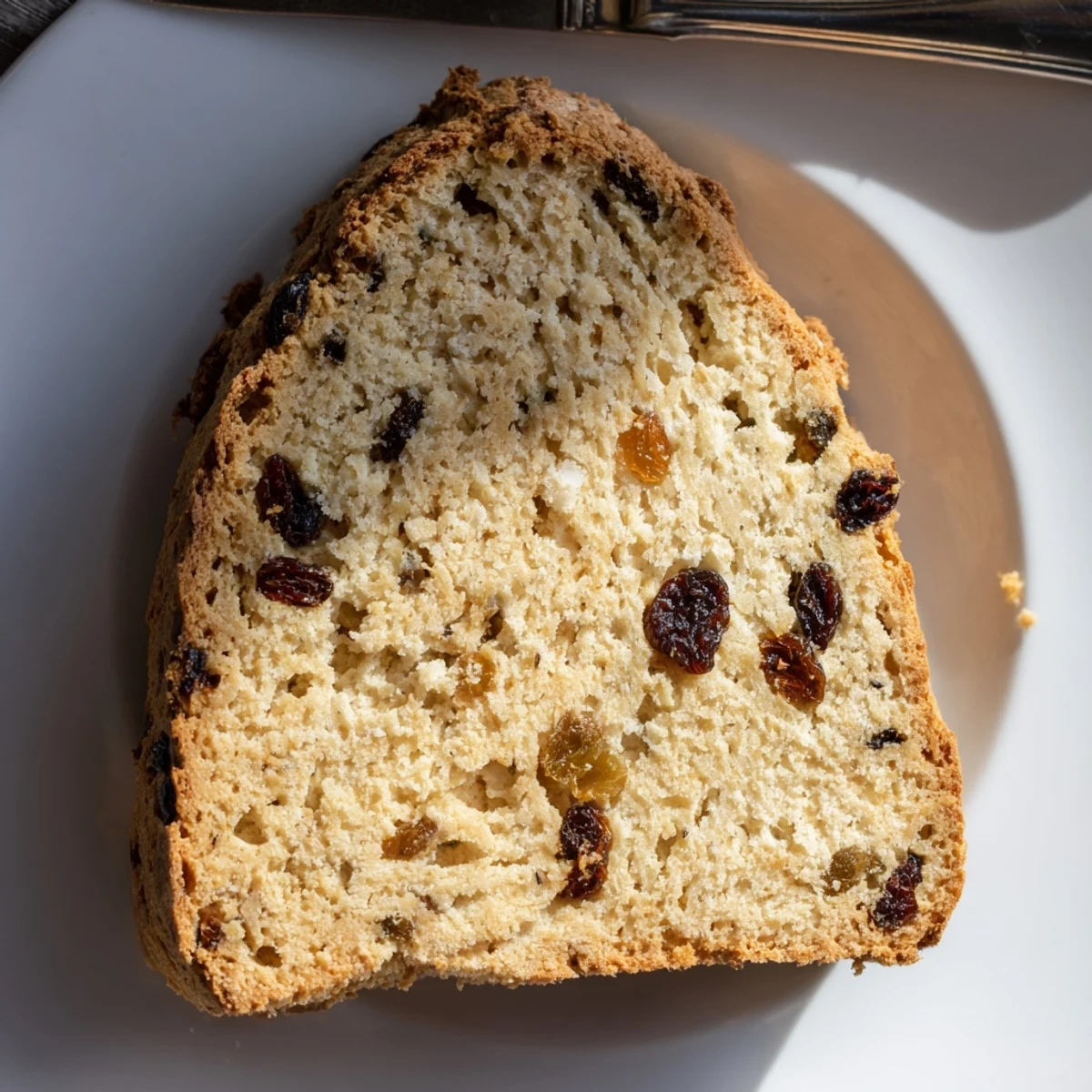 Irish Soda Bread with Currants and Caraway rests on a rustic table, golden crust crackling, with a pat of butter nearby.