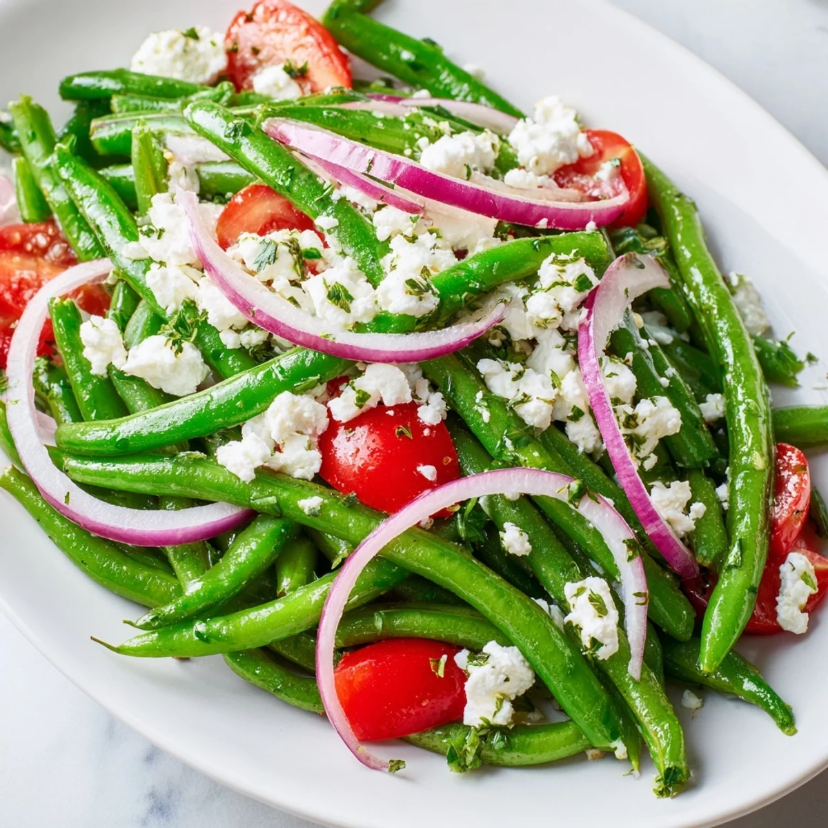 This Mediterranean-inspired Green Bean Salad with Feta features fresh ingredients served on a rustic white plate, ideal as a vibrant side dish for summer barbecues.