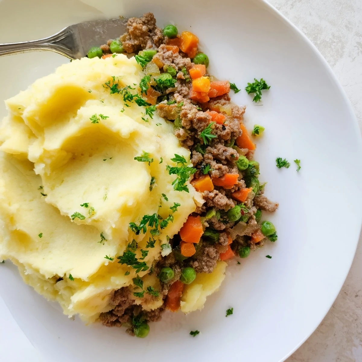 A close-up of golden mashed potatoes, fork-marked peaks, and bubbling ground beef with sweet peas and carrots in Beef Shepherds Pie.  