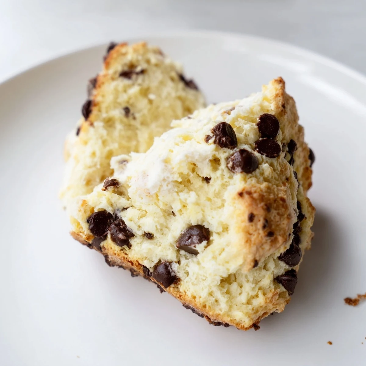 Freshly baked chocolate chip scones resting on a rustic wooden board, their golden edges flaking apart to reveal gooey, melted dark chocolate chunks.
