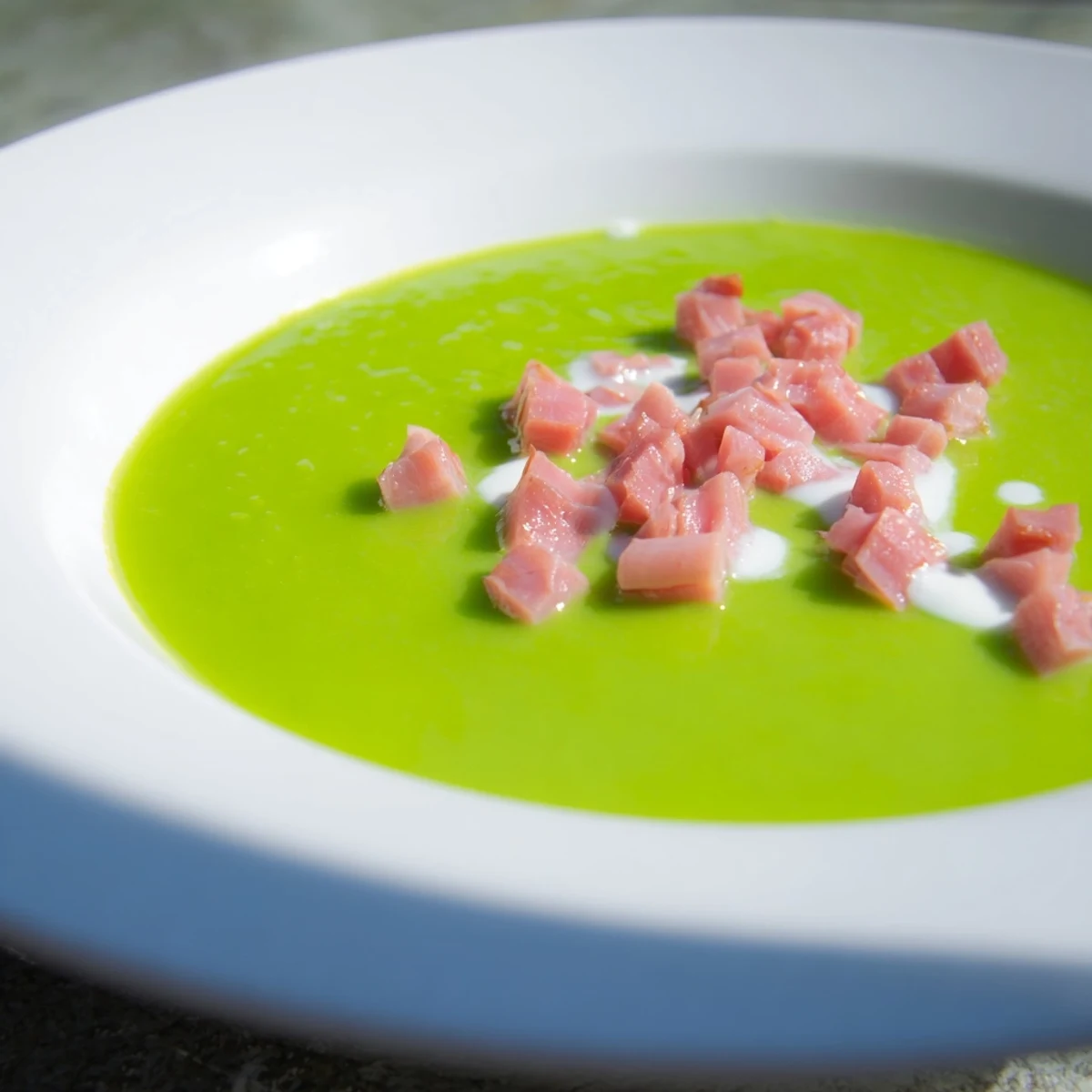 A close-up of vibrant green Spring Pea Soup with Turkey Ham and a slice of crusty bread.