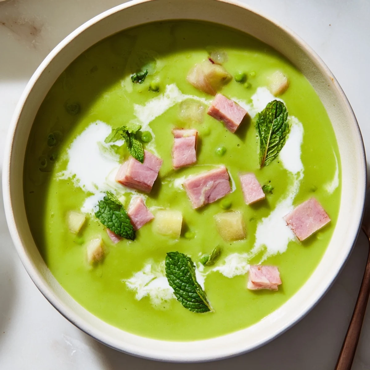 Vibrant Spring Pea Soup with Turkey Ham blended to a creamy consistency, topped with delicate pea shoots and black pepper.