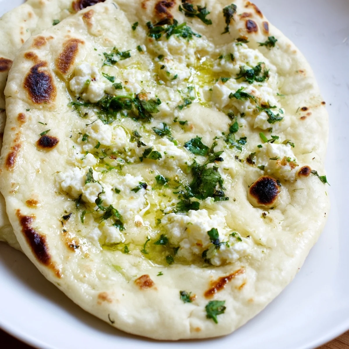 A stack of warm Cottage Cheese Garlic Naan, perfect for scooping up spicy Indian curry or dal on a dinner plate.