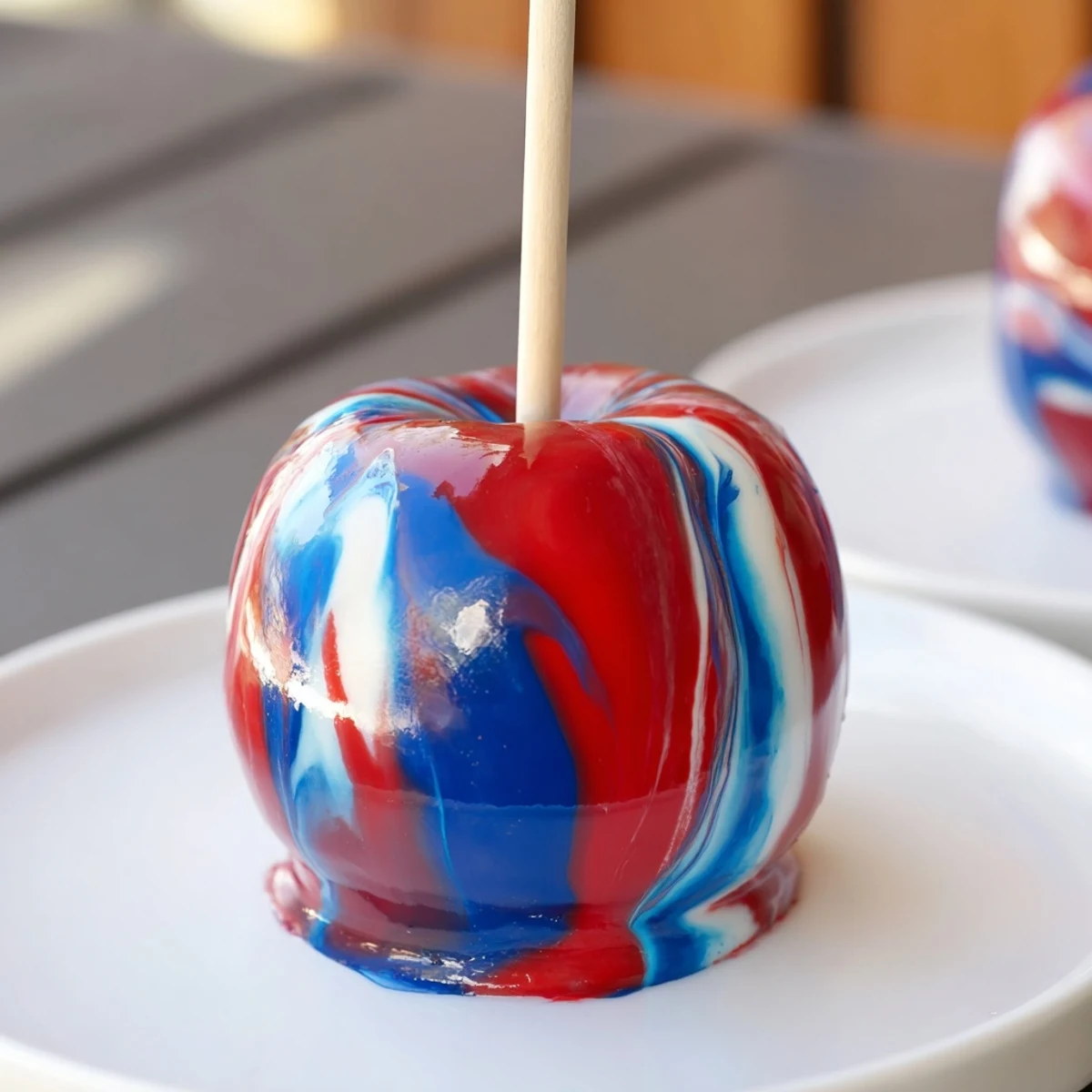 Eight glossy Marbled Effect Candy Apples shine on a white platter with vivid red, blue, and white swirls against a rustic backdrop.