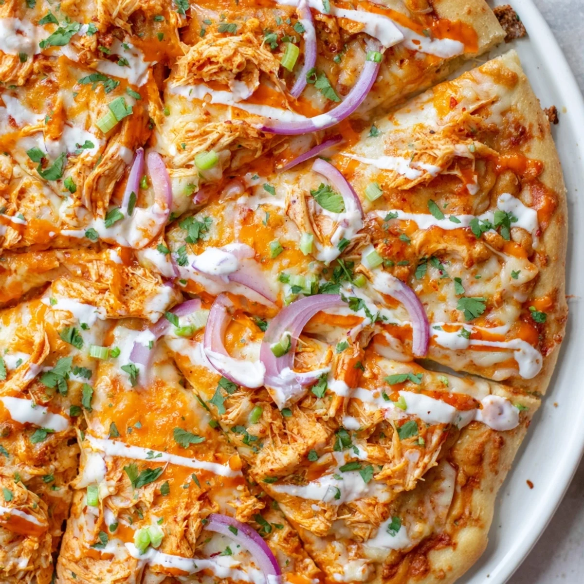 A close-up of Bold Buffalo Chicken Pizza drizzled with ranch and extra buffalo sauce, garnished with scallions and cilantro.