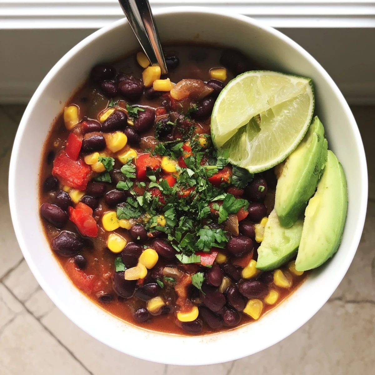 Steaming bowl of Black Bean Corn Chili Lime Delight topped with fresh avocado slices.
