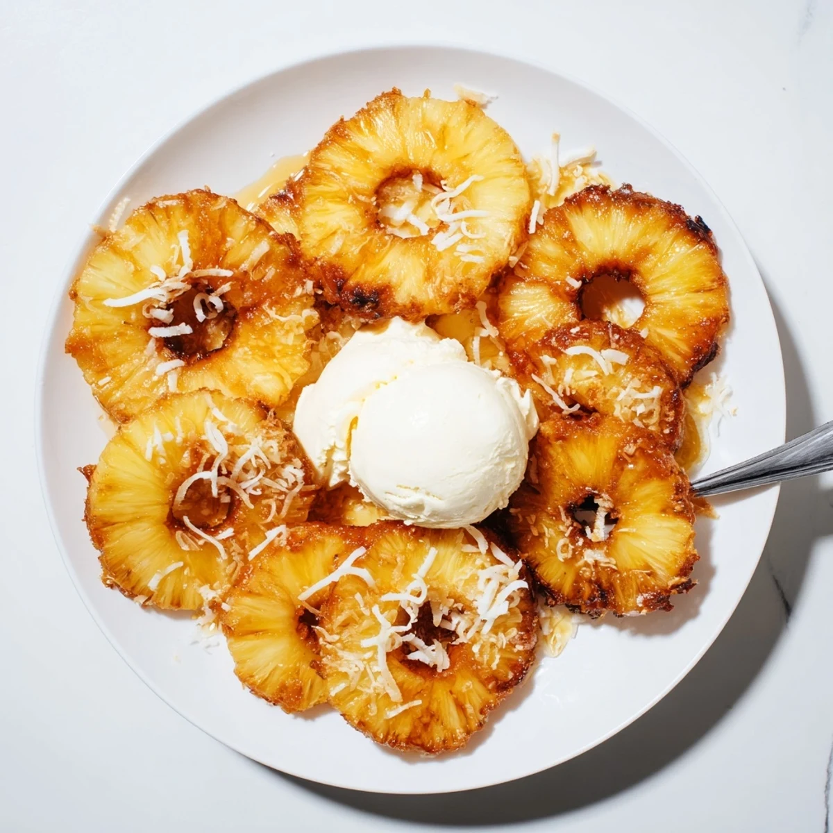 Four servings of Fried Pineapple on a tropical plate with toasted coconut and vanilla ice cream.
