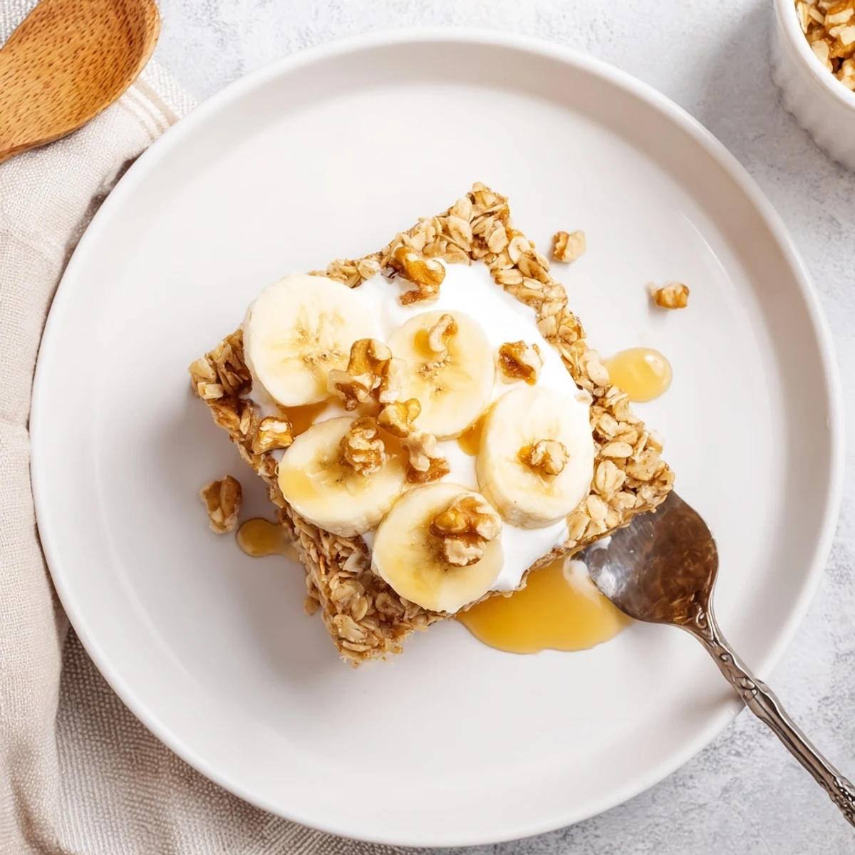 A warm slice of Banana Baked Oatmeal topped with creamy Greek yogurt and sliced bananas for breakfast.