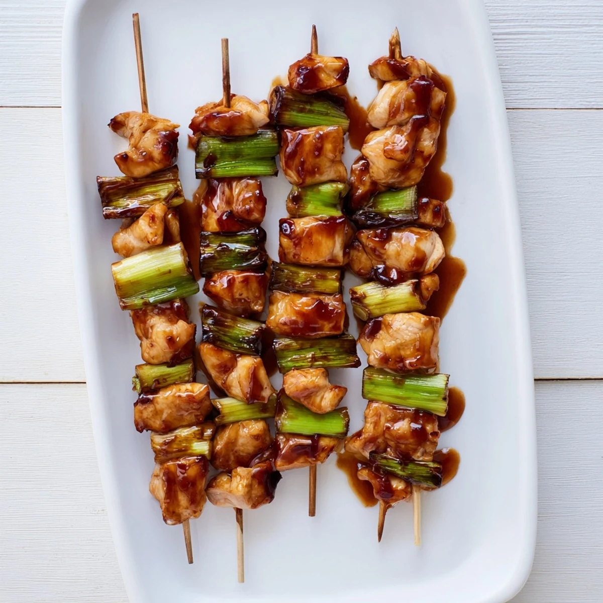 Golden-brown Japanese Chicken Yakitori skewers glistening with tare sauce, served hot off the grill with scallions.
