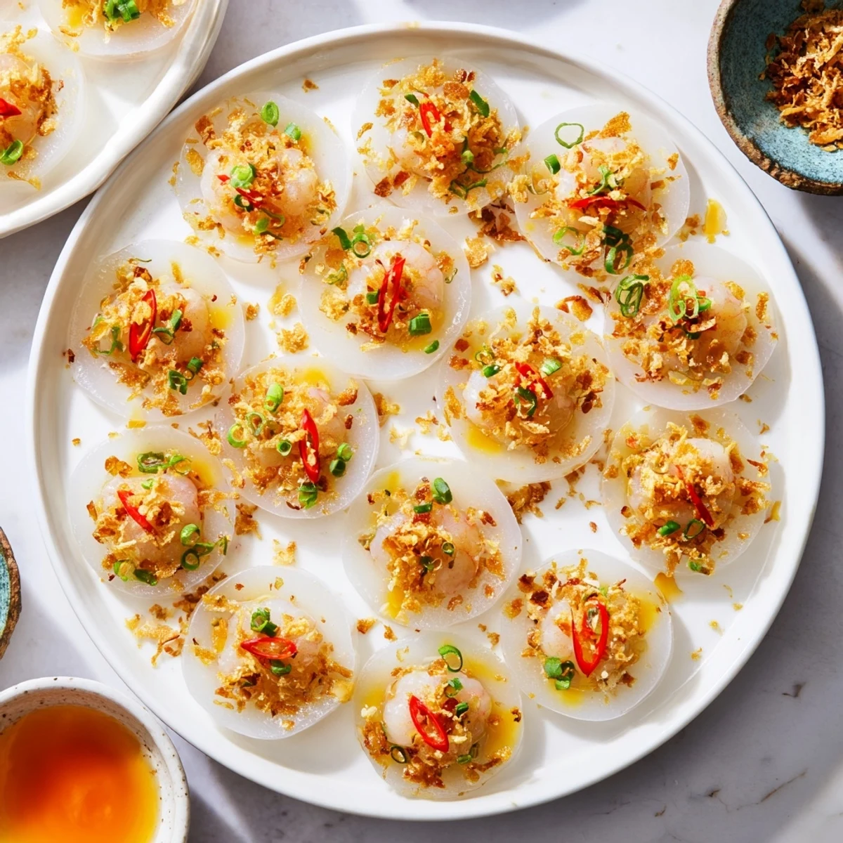Small white Banh Beo steamed rice cakes topped with savory shrimp and fragrant scallion oil in ceramic dishes