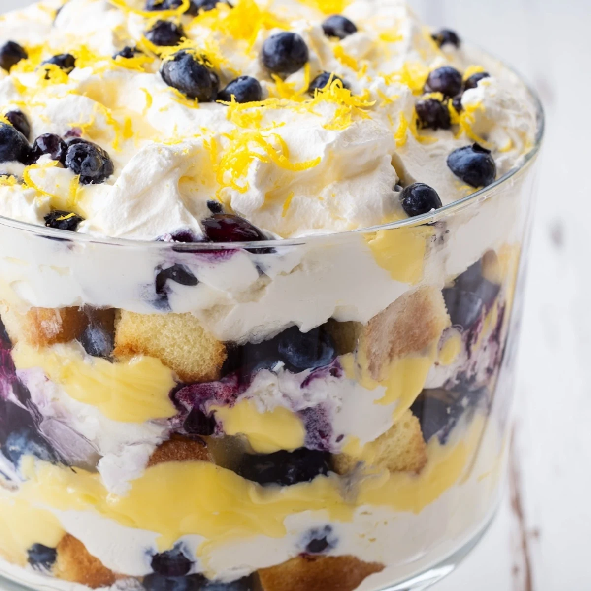 Glass trifle bowl showcasing layered Easy Lemon Blueberry Trifle with creamy whipped topping and fresh blueberry garnish