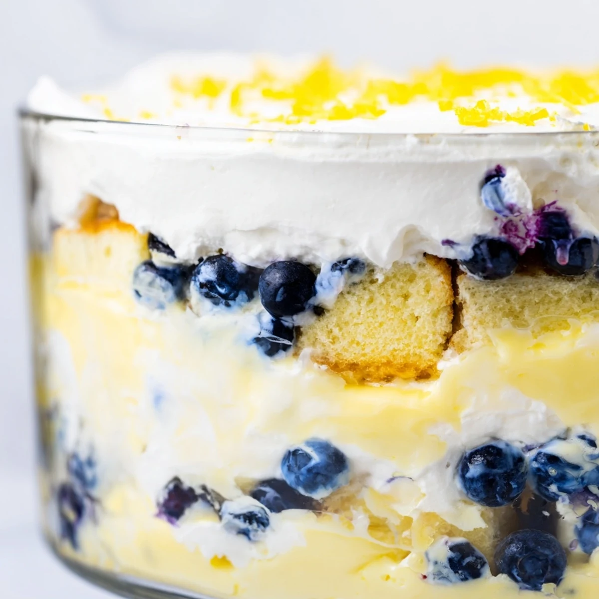 Spoon diving into Easy Lemon Blueberry Trifle revealing cubes of sponge cake nestled between tangy lemon and sweet blueberries
