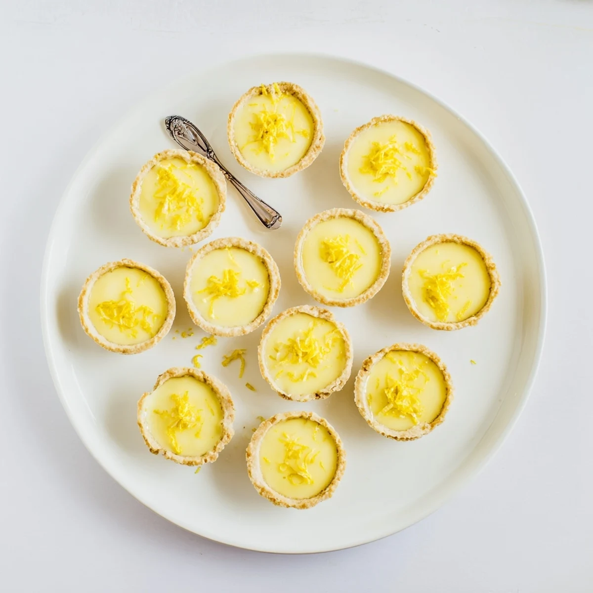 Bite-sized vegan lemon tarts topped with fresh lemon zest on a white serving plate