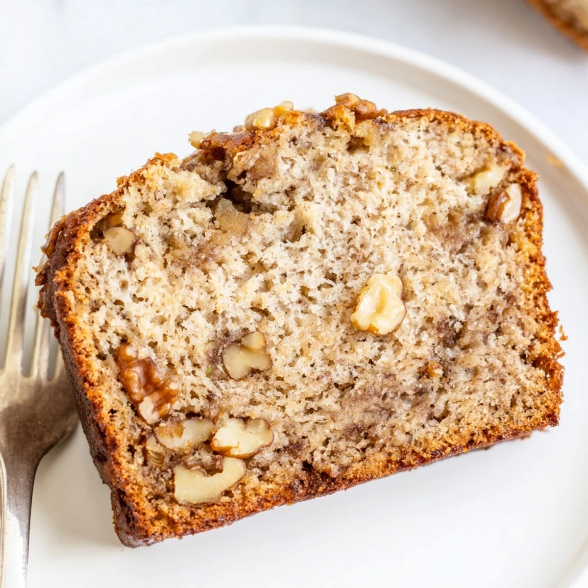 Moist ultimate banana nut bread slice revealing tender crumb and crunchy walnut pieces on a white plate