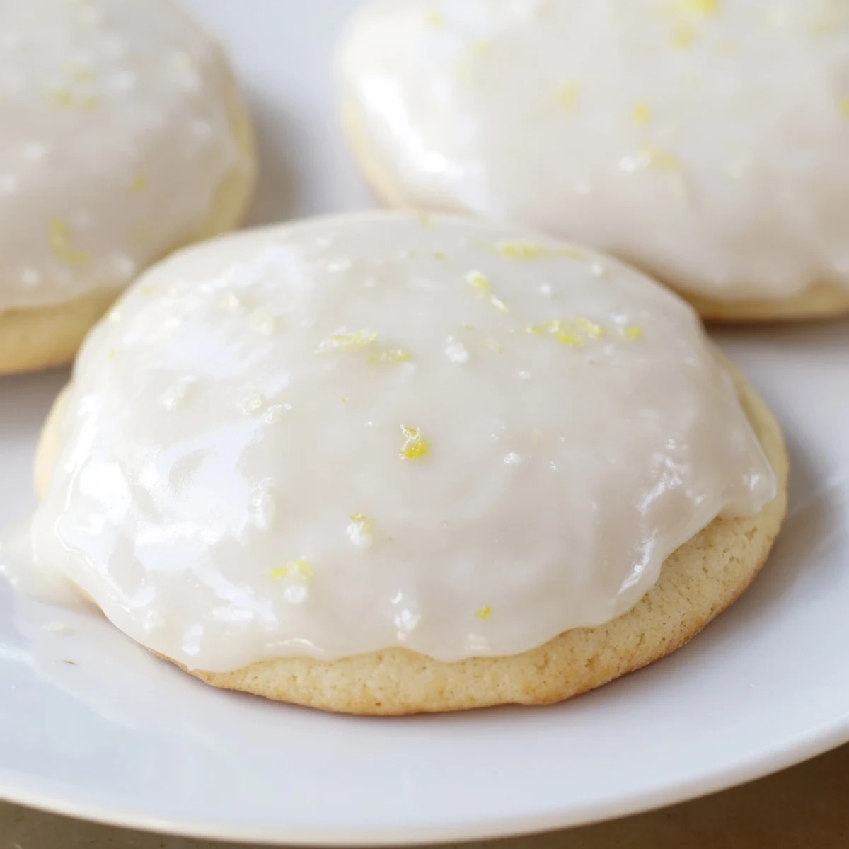 Soft lemon frosted cookies topped with tangy white glaze on a white serving plate