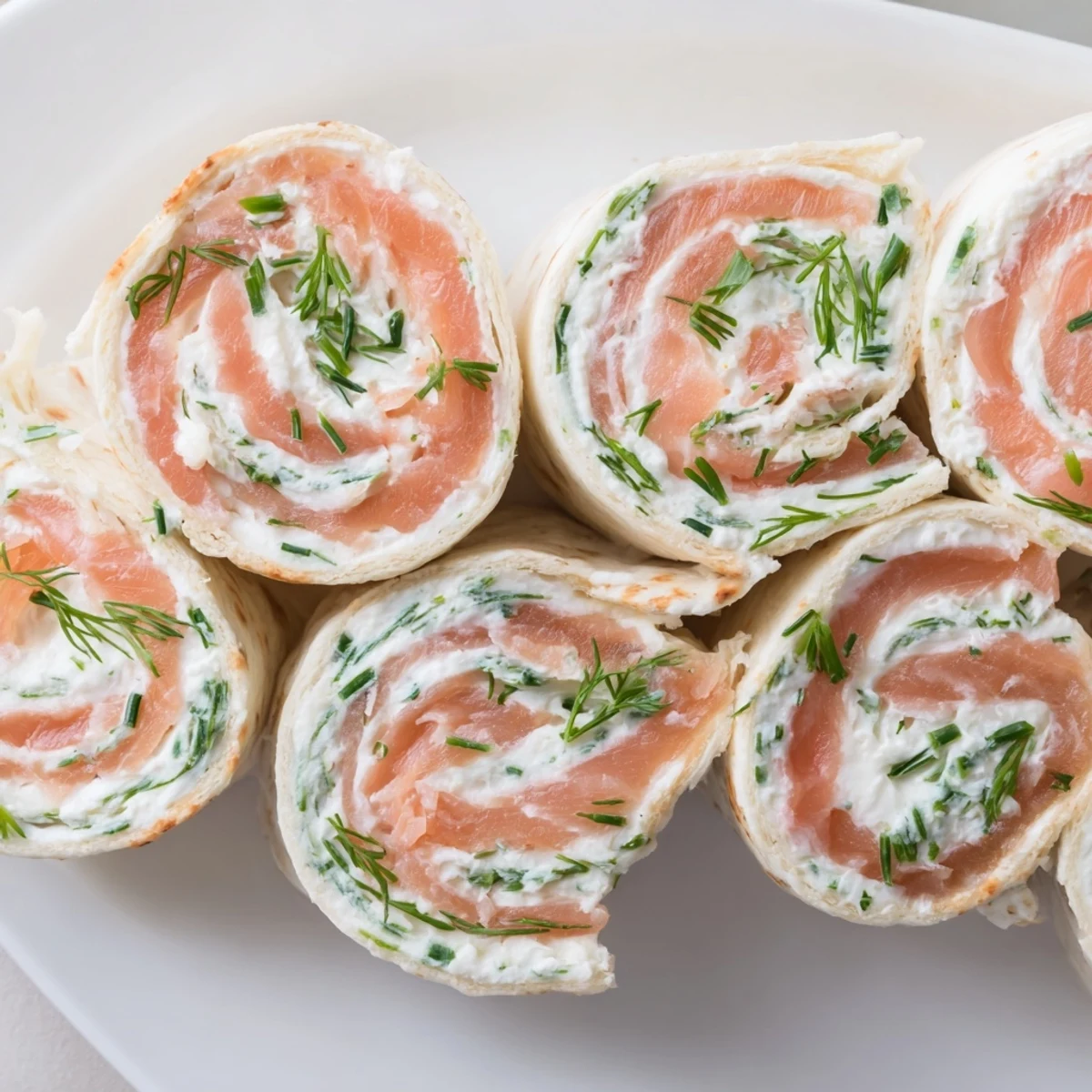 Spiral sliced smoked salmon roll ups with cream cheese and fresh herbs on a white serving platter