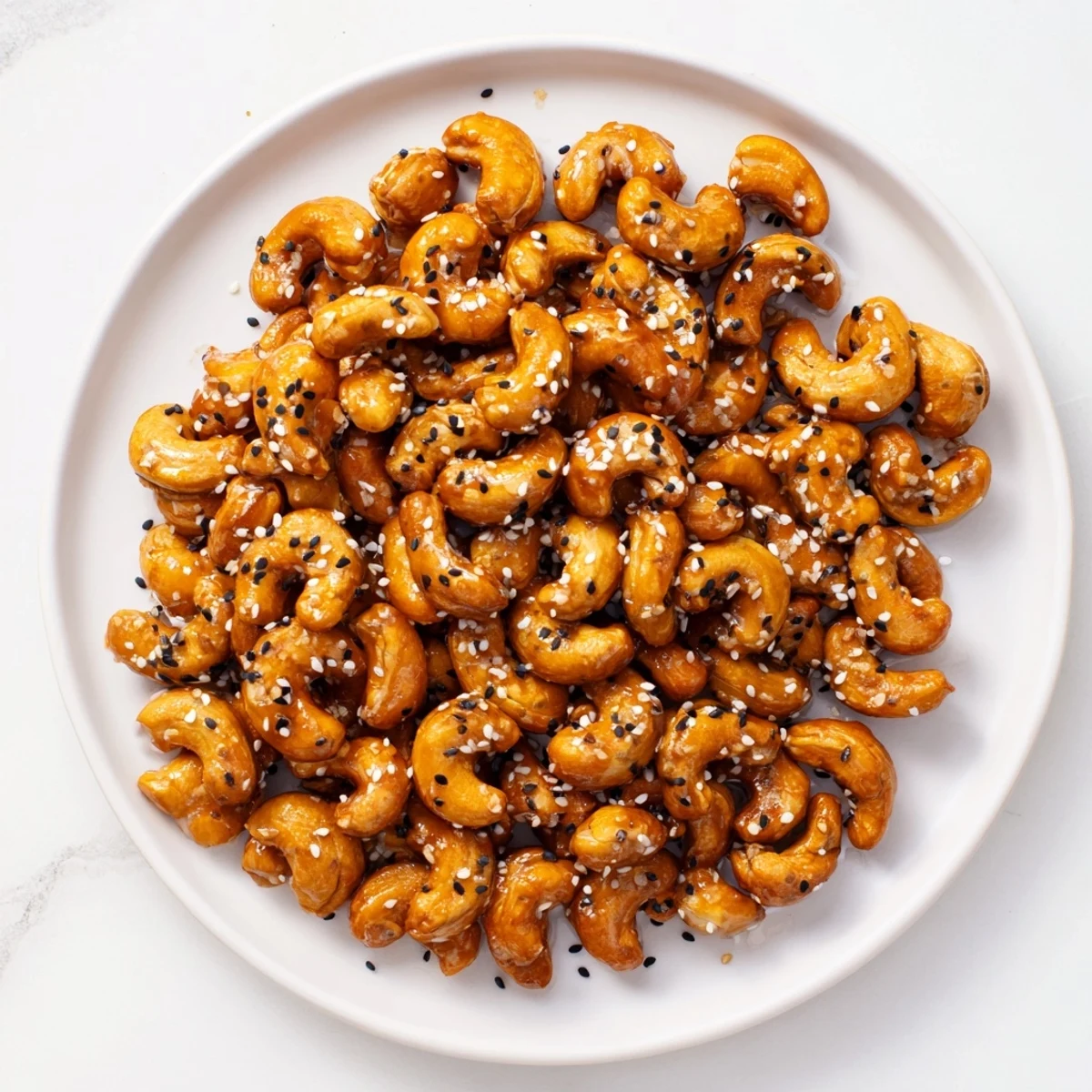 Golden honey sesame cashews scattered on a white serving plate, glistening under warm light