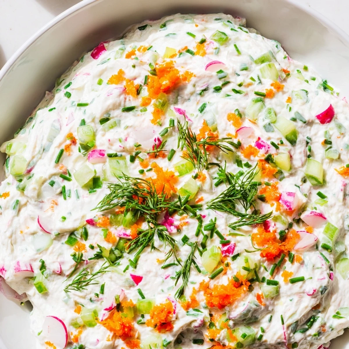 Creamy Easter dip topped with fresh green herbs, grated carrots, and colorful diced vegetables served in a white bowl