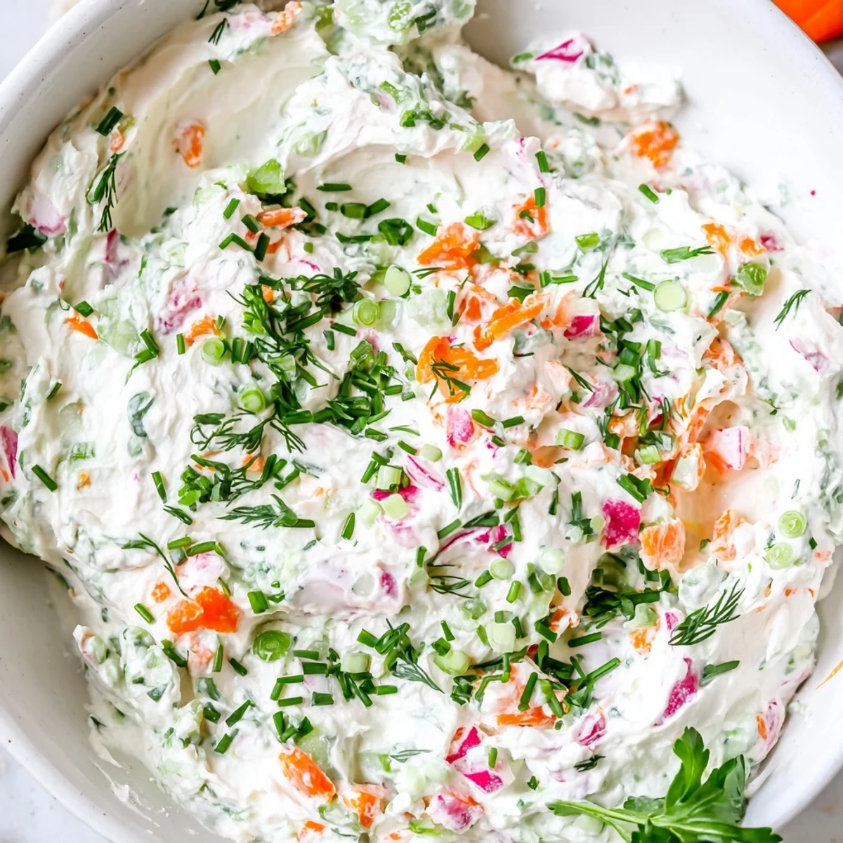 White bowl filled with creamy herb dip garnished with bright orange carrot and crisp cucumber pieces for Easter celebrations