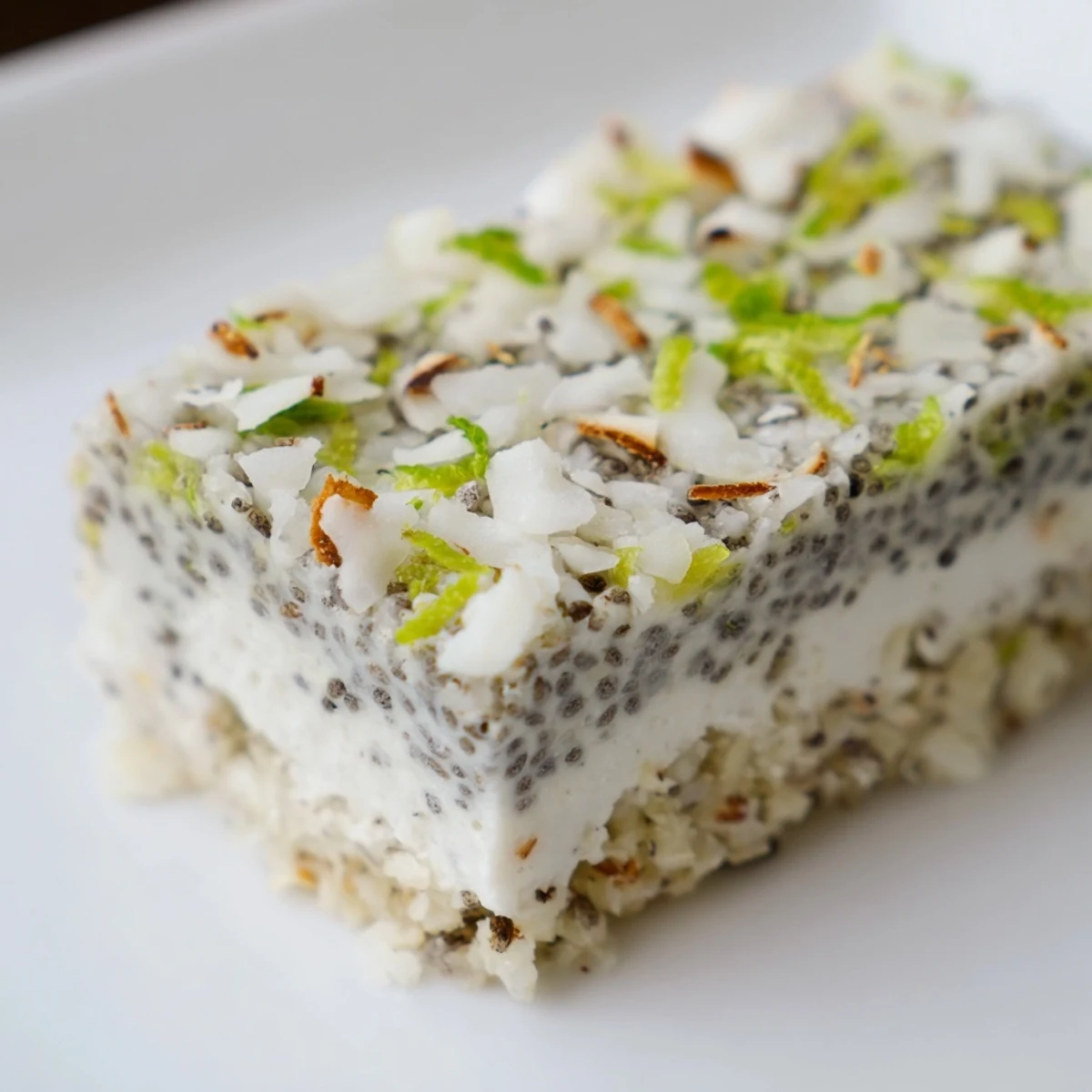 Square slice of no bake zesty coconut lime chia pudding bars topped with toasted coconut flakes and fresh green lime zest