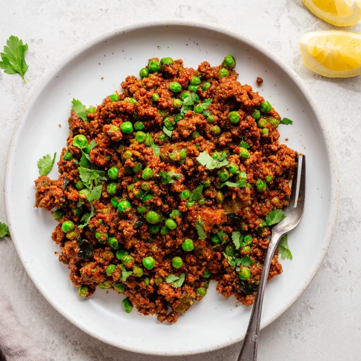 Hearty Savory Keema Curry simmered with tomatoes and spices, garnished with lemon wedges and herbs