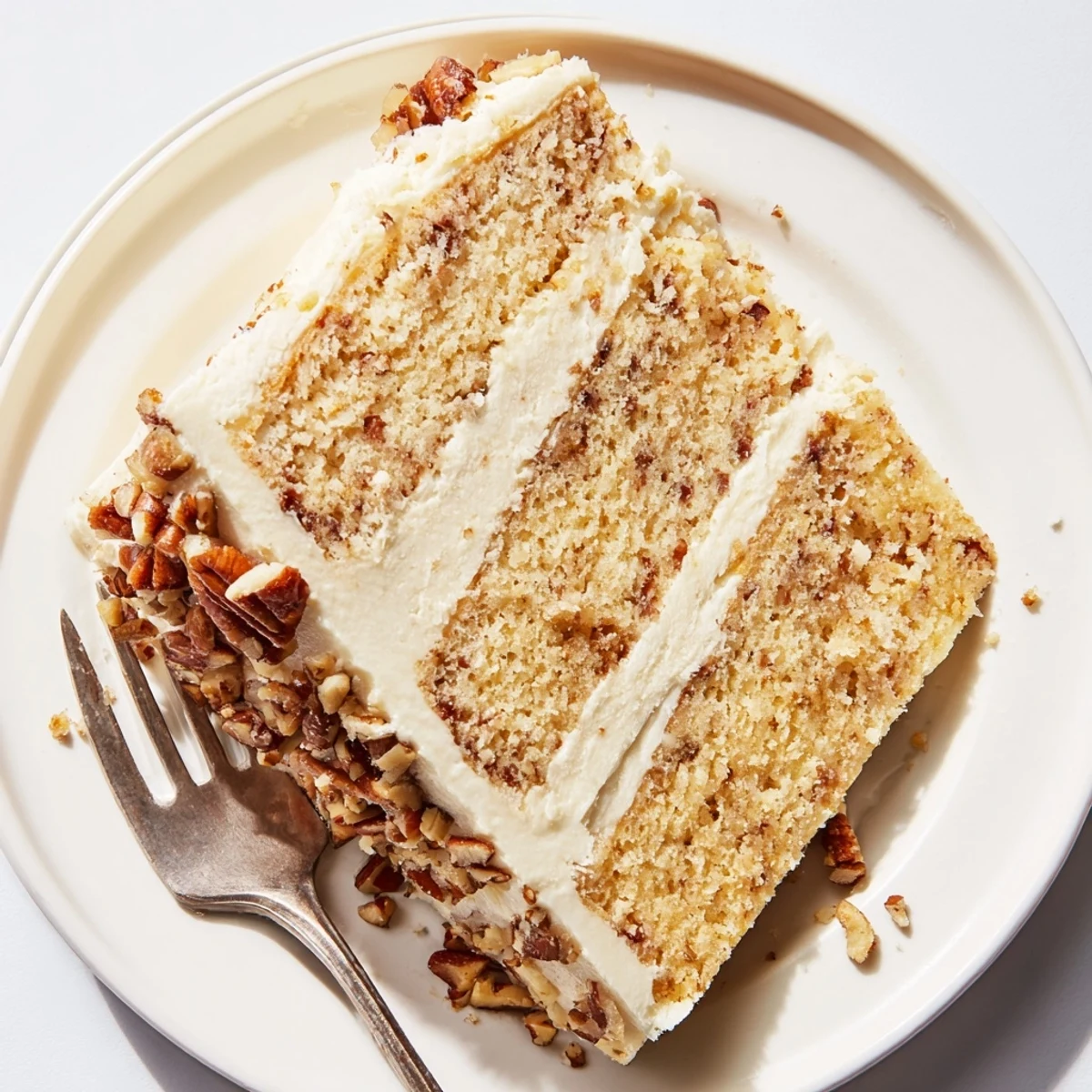 Golden butter pecan cake with velvety frosting and toasted pecan garnish on white plate.