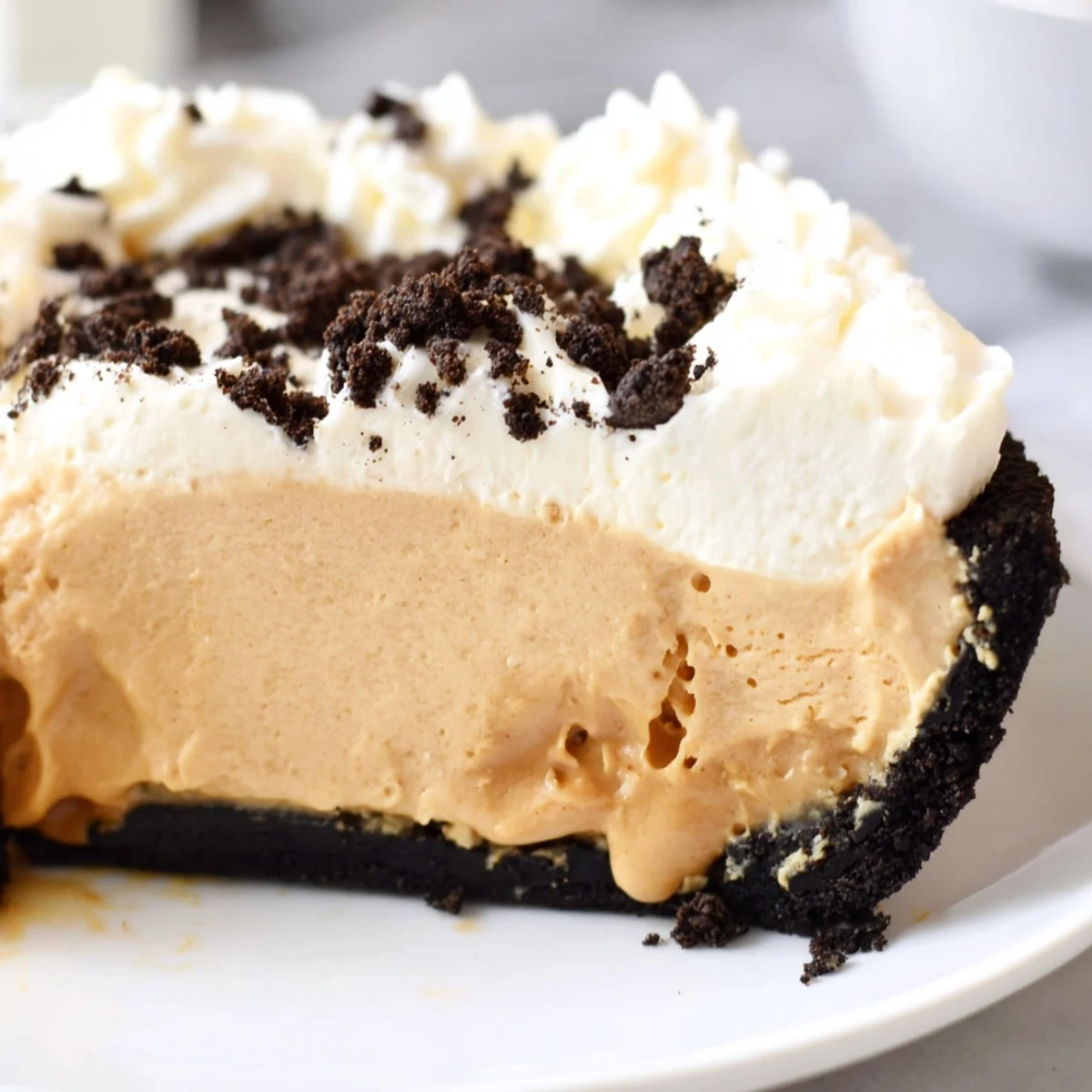 Creamy peanut butter Oreo pie with whipped topping and chocolate cookie crumbles on a dessert plate