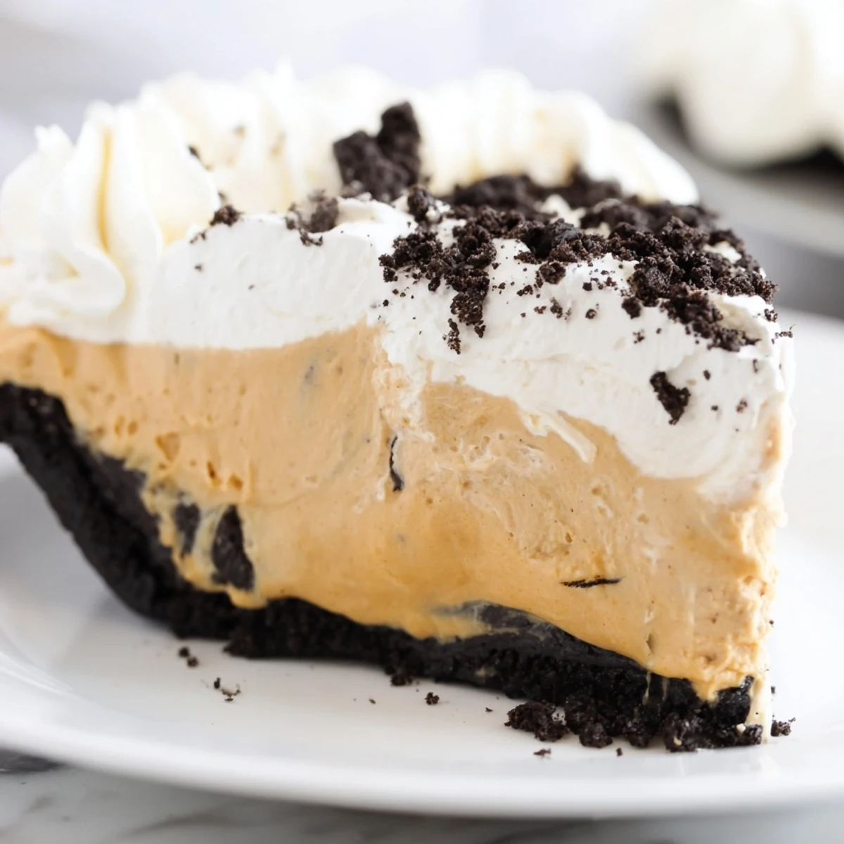 Chilled peanut butter Oreo pie topped with billowy whipped cream and crushed cookies in a glass dish