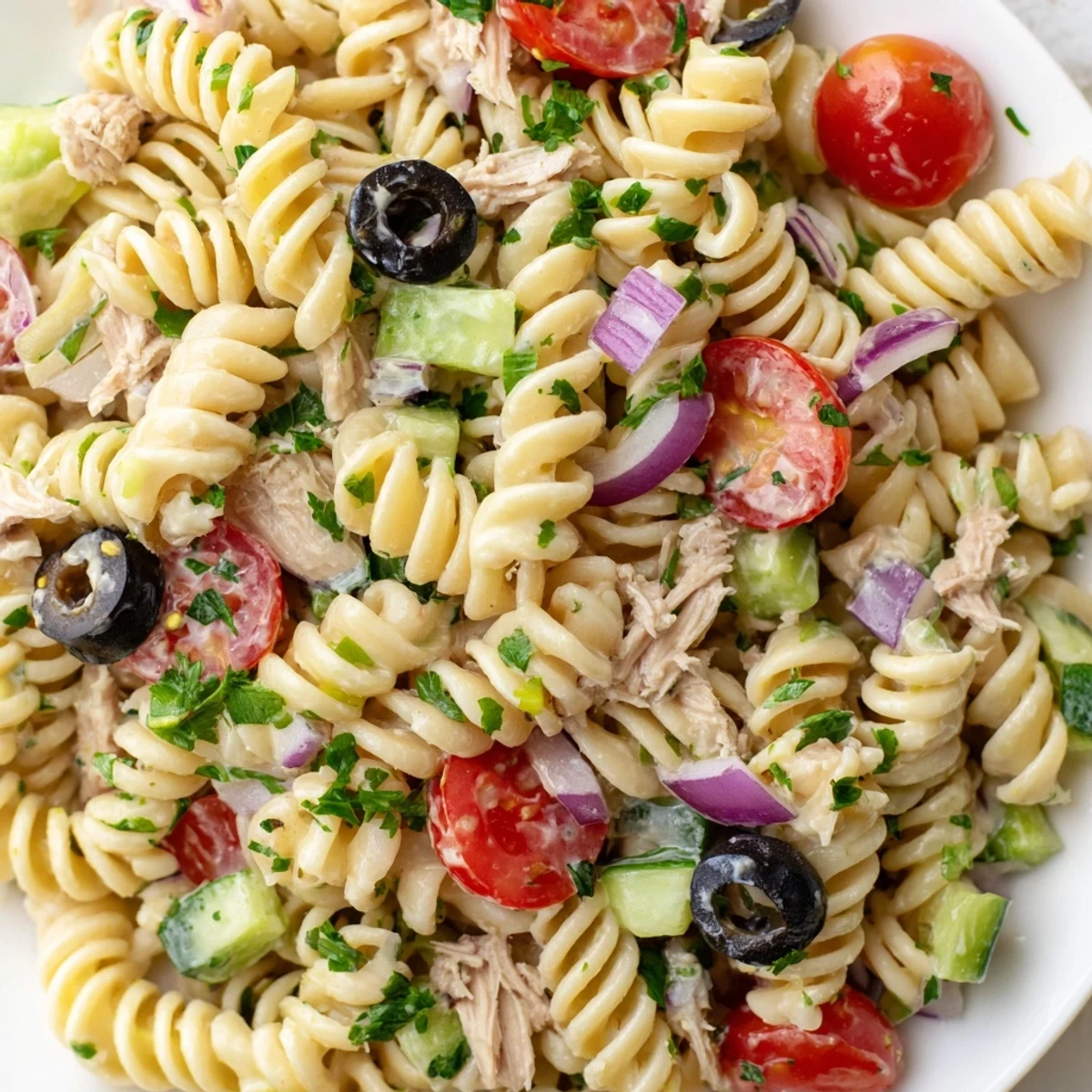 Creamy tuna pasta salad in a white bowl with cherry tomatoes and crisp celery