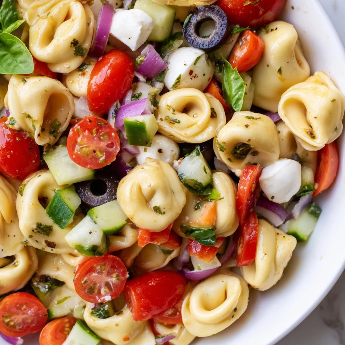 Colorful tortellini pasta salad in a white serving bowl with cherry tomatoes and cucumber