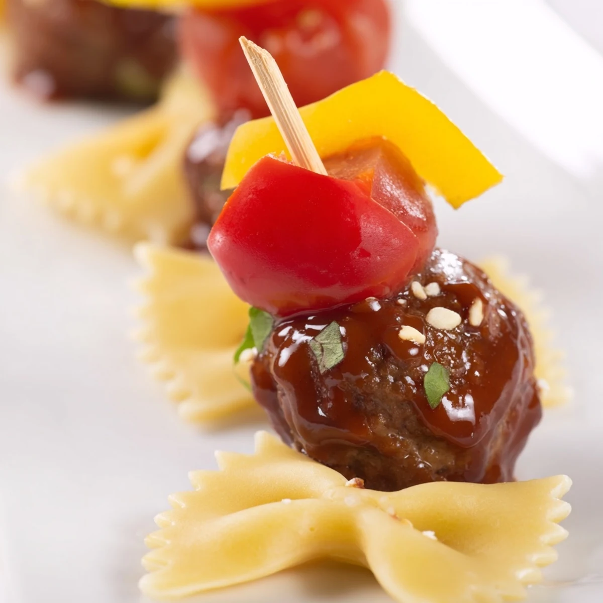 Colorful bowtie pasta and cocktail meatball skewers drizzled with sauce on a platter