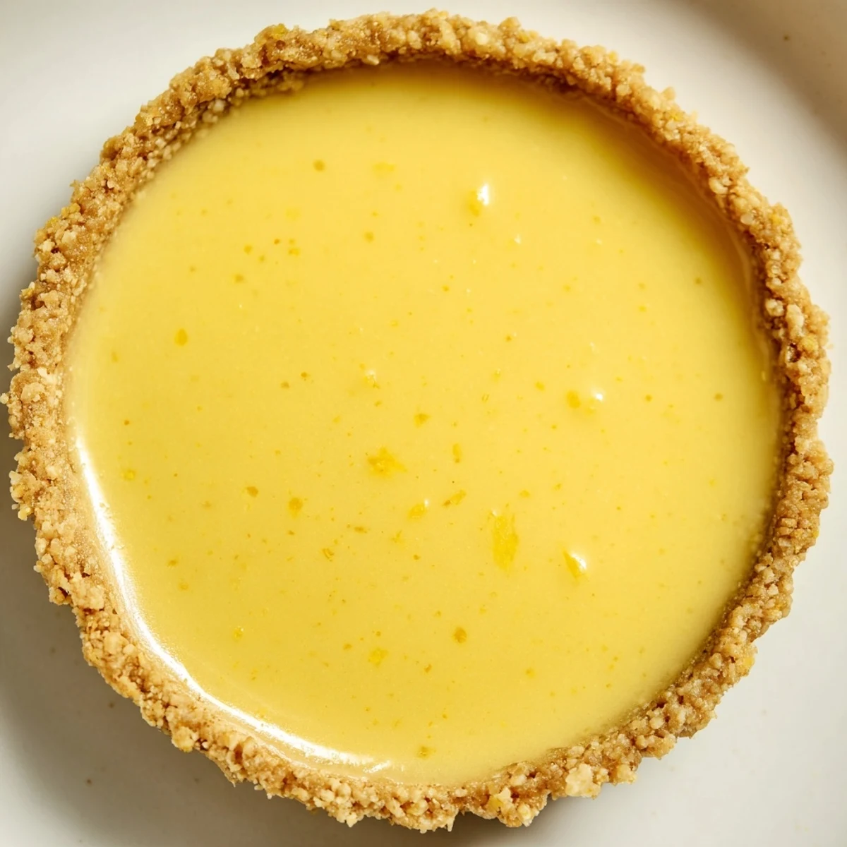 Golden mini vegan lemon tarts topped with fresh berries on a white serving plate