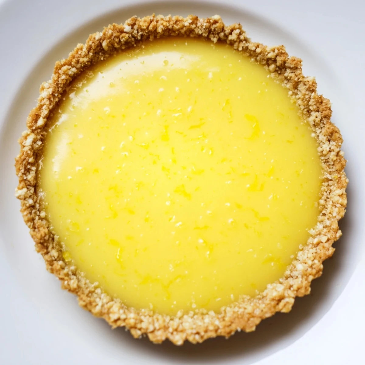 Creamy vegan lemon tarts in crisp almond crusts garnished with delicate lemon zest curls