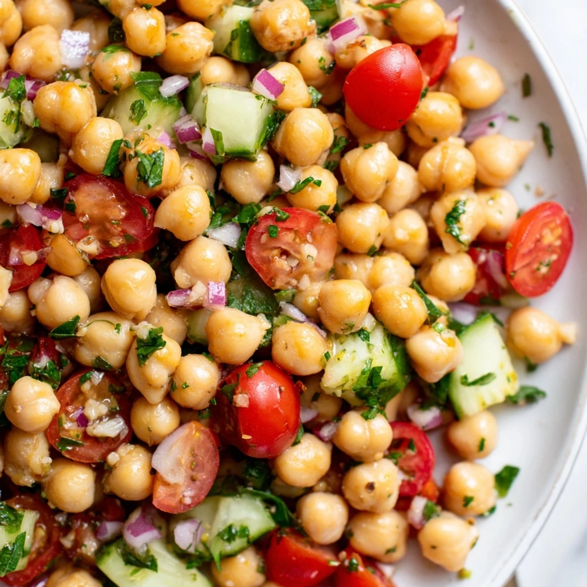 Chickpea cucumber salad in a white bowl with glossy lemon herb dressing drizzled throughout