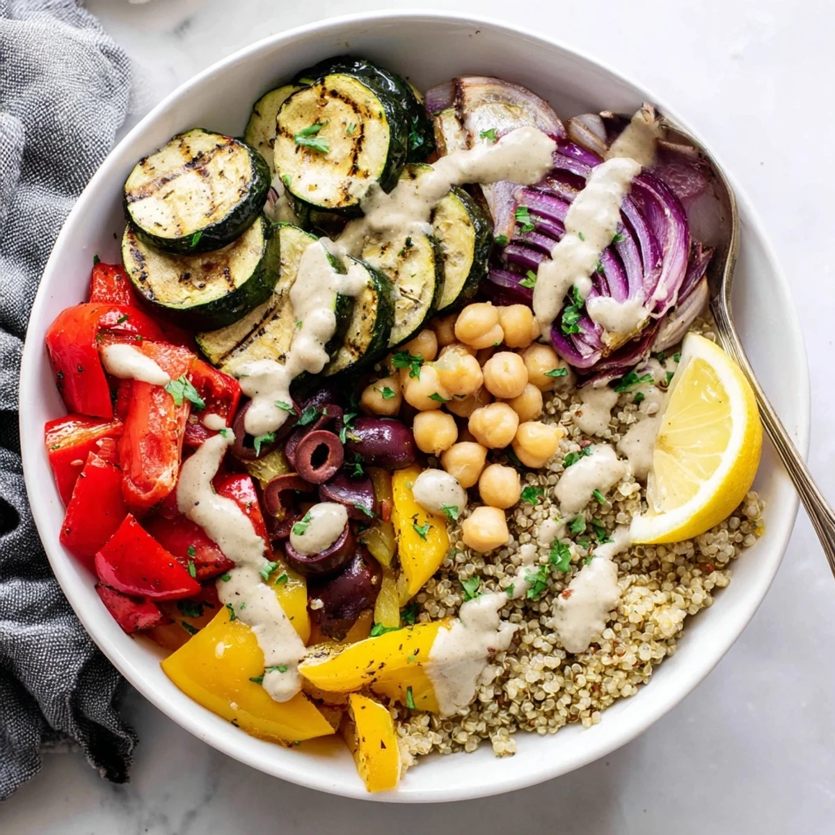 Warm vegan Mediterranean roasted vegetables bowl served over quinoa with zesty lemon tahini and fresh parsley garnish.