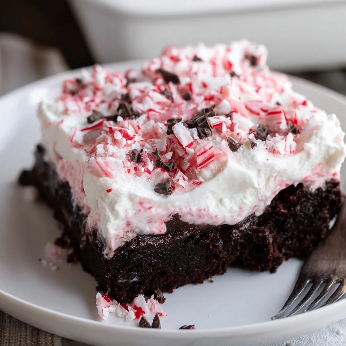 Peppermint Poke Cake topped with fluffy whipped cream and crushed candy