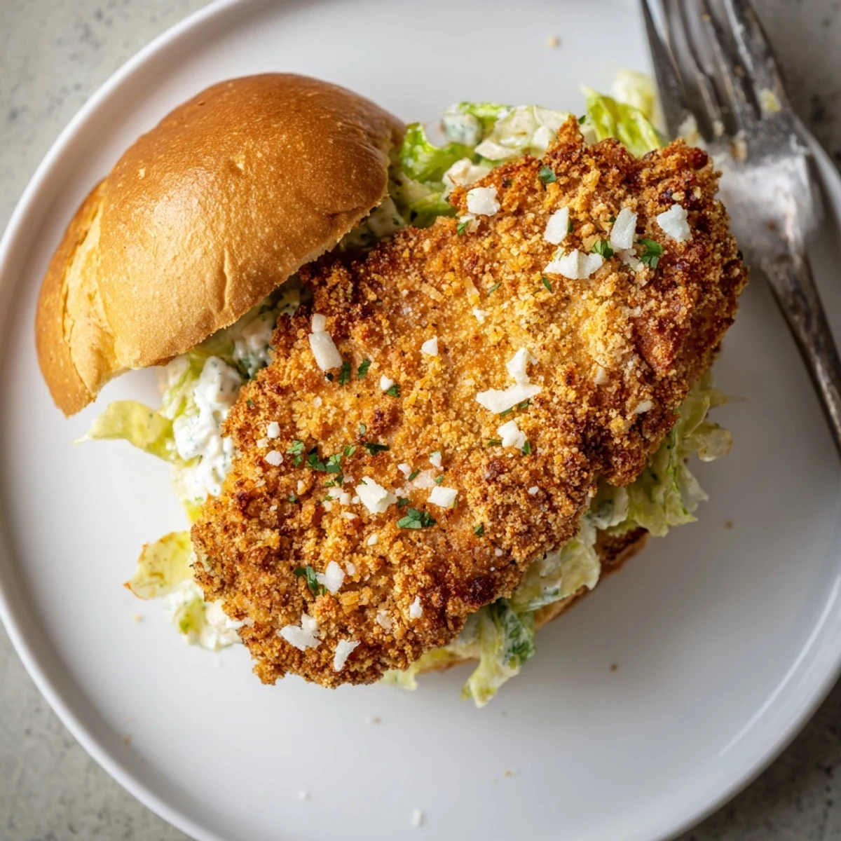 Toasted bun holds Crispy Chicken Caesar Sandwich with creamy dressing and Parmesan