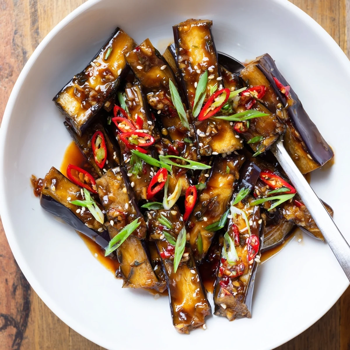 Glistening Sichuan Style Braised Aubergines in spicy red sauce, scallions garnish.