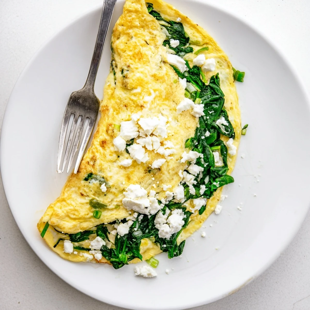 Golden spinach feta omelet folded on a white plate with crumbled cheese topping