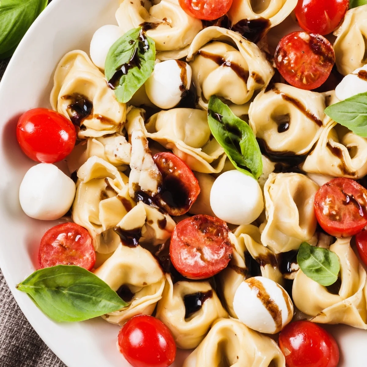 Close-up of chilled tortellini caprese salad showcasing al dente pasta, mini mozzarella balls, and vibrant red tomatoes in olive oil dressing